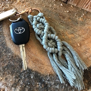 Close-up of handmade grey macrame keychain with cotton tassel and rose gold clasp hardware