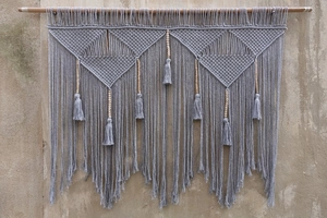 Detail of bohemian gray woven wall tapestry with geometric patterns and wooden beads