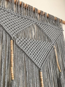Detailed macro view of gray macrame wall hanging with hand-woven knots and wooden beads