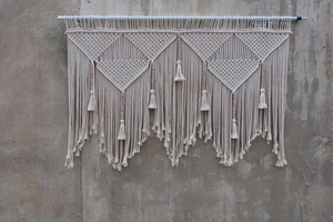 Close-up of bohemian woven wall hanging with white cotton rope, wood beads and fringes