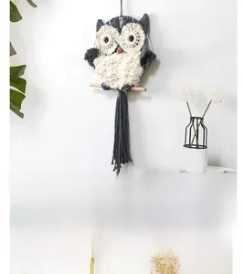 Detail of macrame owl wall hanging with woven fringe and wooden rod on white wall