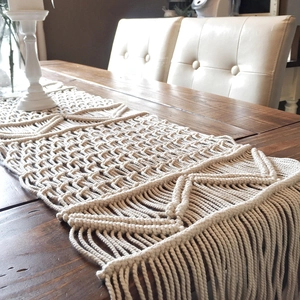 Hand-woven boho table runner with cream cotton ropes and tassels on a wooden dining table