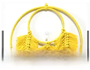 Détail d'une décoration murale jaune tissée main avec double anneau et pompons en coton