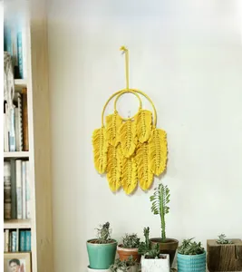 Détail d'une suspension murale en macramé jaune avec sept plumes tissées à la main en coton