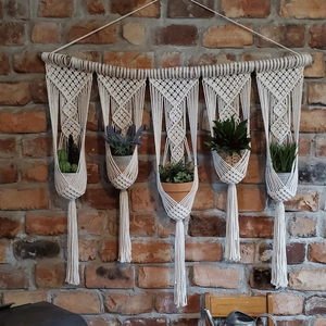 Detail of macrame plant hanger with five pockets and natural wood stick on brick wall