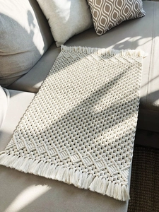 Detail showing handwoven cotton rope texture with bohemian fringes on a grey sofa