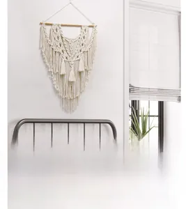 Détail d'une décoration murale en macramé bohème avec pompons en coton et tige en bois