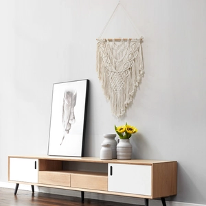 Handmade boho macrame wall hanging with geometric weave and tassels on white wall