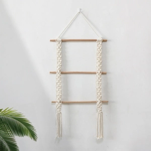 Handmade boho macrame wall hanging with three-tier wooden shelves on a white wall