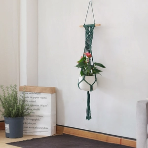 Detail of hand-woven cotton macrame plant hanger with wooden rod and white ceramic flower pot