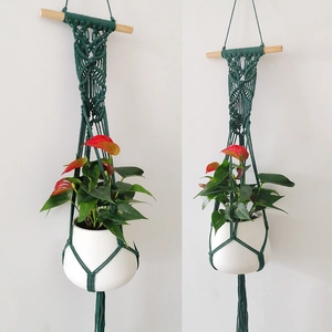 Detail of green handmade macrame plant hanger with cotton rope weaving and wooden stick