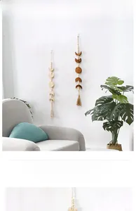 Detail view of boho wooden moon phase wall hanging with cotton tassels on white wall