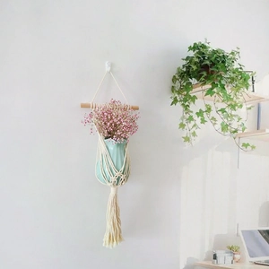 Detail of macrame plant hanger with blue ceramic vase and pink flowers on white wall
