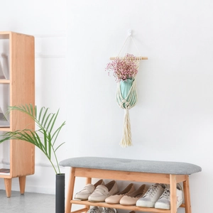 Close-up of handmade macrame plant hanger with cotton rope and pink flowers on white wall