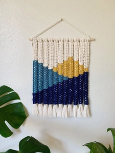 Handmade macrame wall hanging with geometric mountain scenery and white cotton tassels
