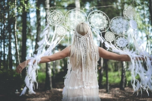 Detail van de bohemian witte gehaakte hoofdband met veren in een zonnig bosdecor