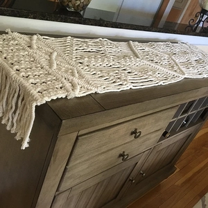 Handmade Macrame Table Runner with boho woven patterns and long fringe on wooden cabinet