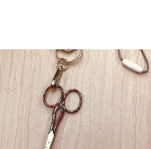 Miniature portable metal scissors pendant with red and black enamel on wood surface