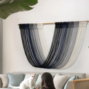 Nordic woven macrame wall hanging with blue and gray fringe over a sofa on white wall