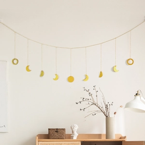 Detail of moon phase gold metal wall hanging with 11 pendants on a beige wall