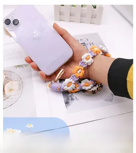 Macro detail of hand-woven floral phone wrist strap with metal hook on purple smartphone