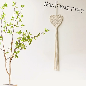 Detail of hand-knitted heart wall hanging with natural cotton fringe in minimalist interior