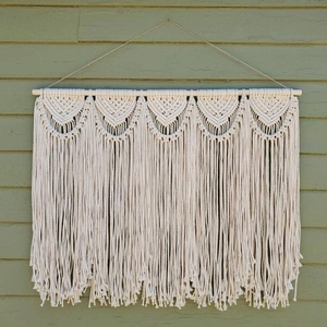 Detailed close-up of handmade macramé wall hanging with beige cotton ropes and wood rod
