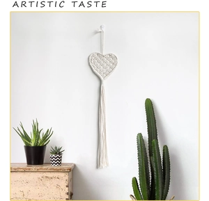 Detail of bohemian handmade heart-shaped woven tapestry with tassels on white wall