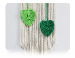 Detail of handmade macrame wall hanging with green woven leaves and cotton tassels