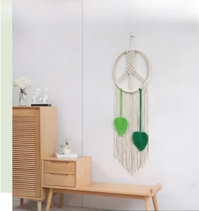 Detail of hand-woven macrame wall hanging with wooden ring and green leaf accents