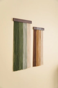Detail of bohemian wall hanging featuring handwoven cotton tassels on a dark wood rod