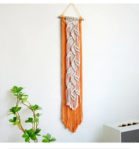 Close-up of bohemian leaf macrame wall hanging with orange tassels on white wall