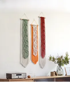Detail of bohemian woven wall hanging featuring three leaf fringe tassels on a wooden rod