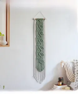 Close-up of Bohemian hand-woven wall hanging with sage green leaf fringe and wood rod