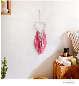 Detail of bohemian handmade heart-shaped woven wall hanging with soft pink and white tassels
