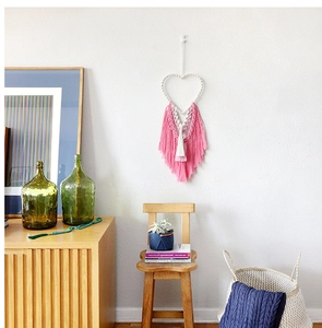 Detail of bohemian heart-shaped macrame wall hanging with pink and white cotton tassels