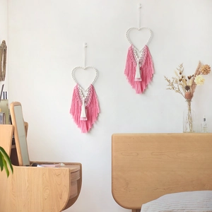 Bohemian heart-shaped macrame wall hanging with pink fringe and woven feathers