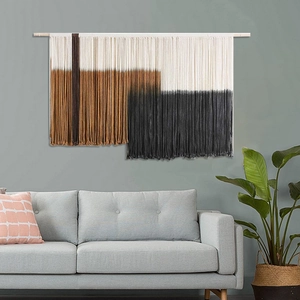 Nordic handmade woven tapestry with tassels hanging above a sofa on a blue wall