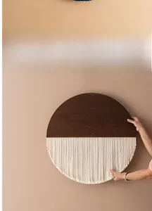 Detail eines runden Wandbehangs im Boho-Stil mit dunklem Holz und cremefarbenen Quasten