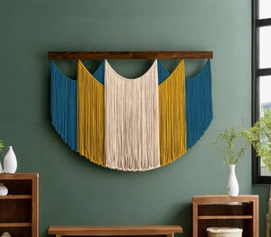 Detail of bohemian woven tapestry with blue and yellow tassels on dark green wall