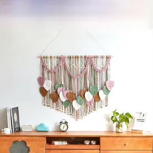 Detail of bohemian leaf tapestry with pink and sage green tassels on a wooden rod