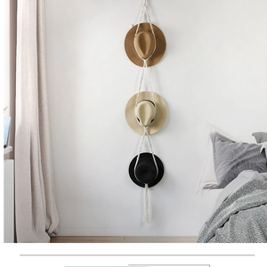 Detail view of handmade macrame hat hanger with fringe accents on a white wall