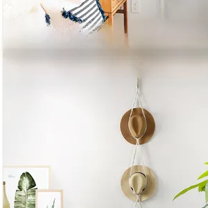 Detail view of woven cotton rope hat organizer with two wide-brimmed straw hats on white wall