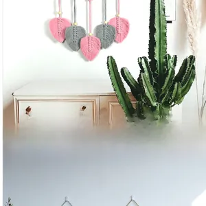 Détail d'une décoration murale en macramé avec des feuilles tissées en coton rose et gris