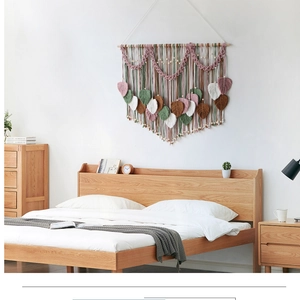 Detailed close-up of handmade macrame leaf tapestry with wooden beads on a white wall