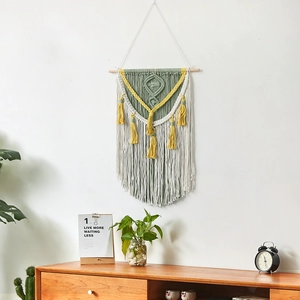Handmade macrame wall hanging with green and yellow tassels on a wooden pole