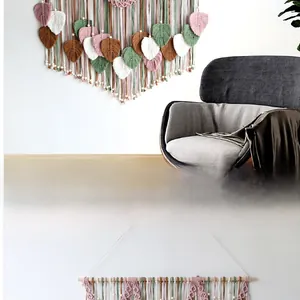 Detail of handmade macrame leaf tapestry in pink green and white on wooden pole