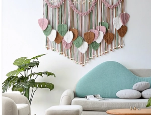 Detail of bohemian handmade woven wall hanging featuring cotton leaf feathers and wooden beads