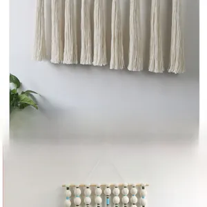 Detailed close-up of bohemian hand-woven wall hanging with cotton tassels and wooden rod