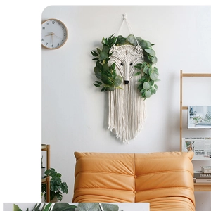 Detail of fox head woven macrame tapestry with eucalyptus leaves on a white wall
